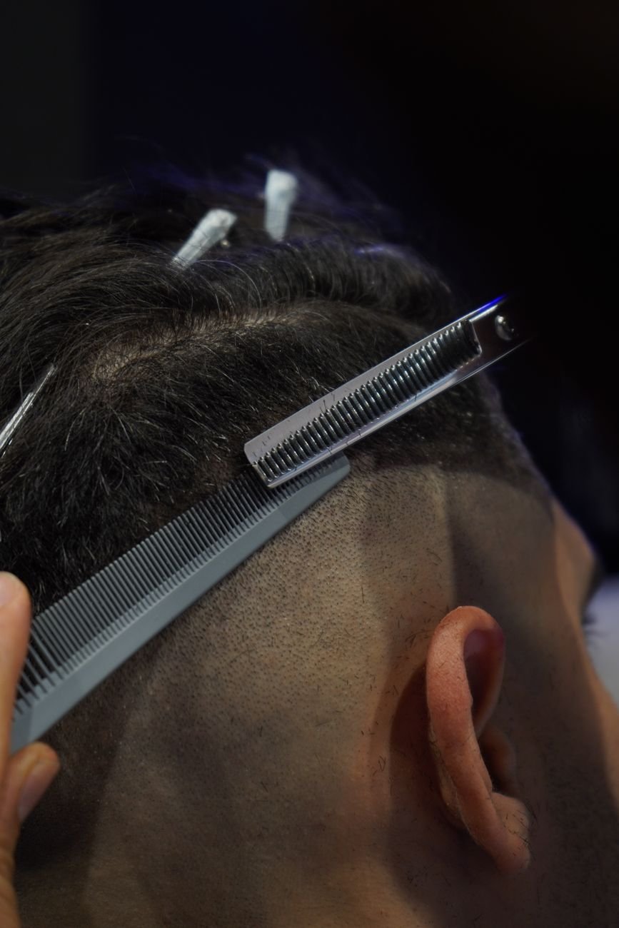 Close-up of a professional haircut in progress with comb and scissors in a barbershop setting.