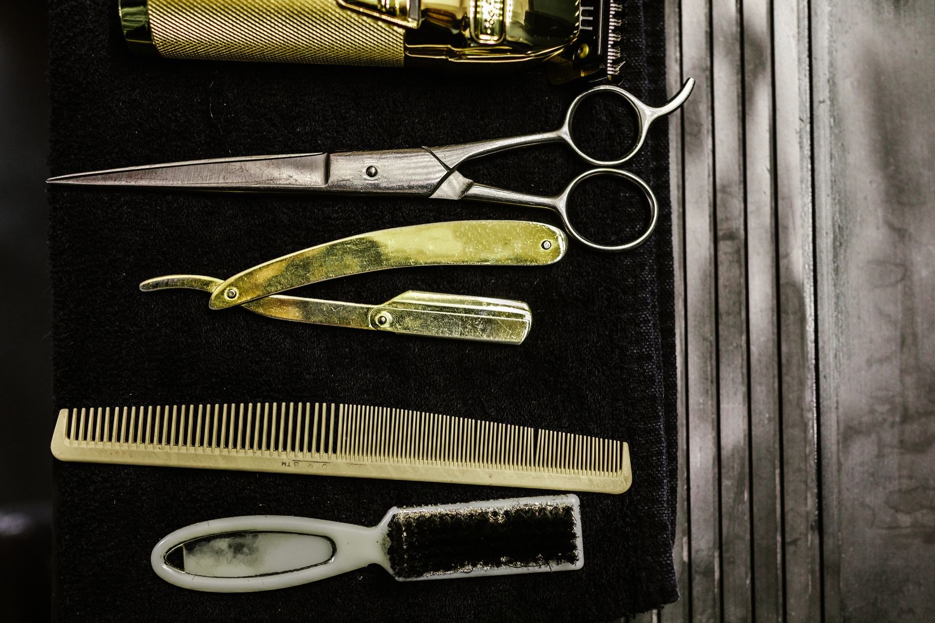 A set of vintage barber tools including scissors, razor, comb, and brush on a dark background.